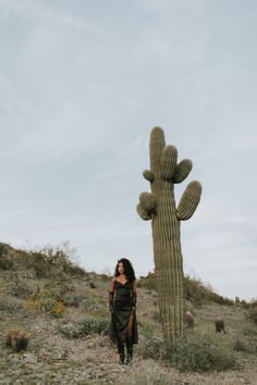 a woman standing next to a tall cactus