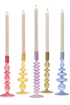 four candles are lined up in different colors and sizes, each with a candle holder