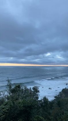 an ocean view with trees and the sky covered in clouds