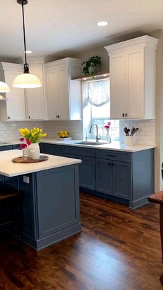 a large kitchen with white cabinets and blue island in the center is decorated with yellow tulips