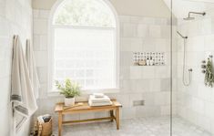 a white bathroom with a wooden bench and shower