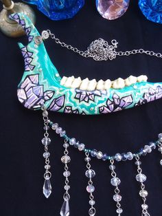 This is a Beautiful Painted,Turquoise Crystal Deer Jawbone Necklace! The Colors Here Are Just Fantastic! The Painted crystals Are a Light Purple Color And The Backdrop is Turquoise! A few rhinestones as well. Hanging from the bottom is a String of Glass beads! All 6 Teeth Are in perfect condition. The Whole Jaw Bone is 9 inches long. Also coated with polyurethane for the beautiful shine. The Chain is 20 inches long. All Items Ship Within 1-3 Days via USPS First Class Service. Shipping on This Bo Unique Handmade Bone-colored Necklace, Handmade Bone-colored Unique Necklace, Unique Handmade Bone Necklace, Bohemian Bone Colored Jewelry For Festivals, Bohemian Bone-colored Necklace For Festivals, Bohemian Bone-colored Jewelry For Festival, Painted Crystals, Real Bone Jewelry, Wiccan Necklace