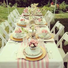 a long table set with plates, cups and utensils for an outdoor dinner