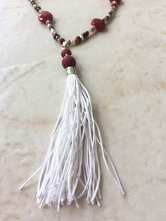 This handmade necklace and earrings set is made from a handmade white tassel with red dyed wood beads; semiprecious red jade faceted teardrops; glass seeds beads in brown, burgundy red, and white; and silver-tone components. White Tassel Jewelry For Festival, Festival White Jewelry With Tassels, Festival White Tassel Jewelry, White Beaded Necklaces With Tassels As Gift, White Beaded Necklaces With Tassels For Gift, White Beaded Tassel Necklaces As Gift, Red Tassel Necklaces As Gifts, Red Tassel Necklaces For Gifts, Red Tassel Necklace For Gift