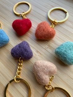 four different colored felt heart keychains on a wooden surface with two gold rings