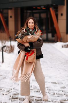 a woman is standing in the snow with her arms crossed and holding a bouquet of flowers