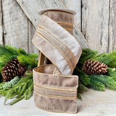 two rolls of ribbon on top of evergreen branches and pine cones in front of an old wooden wall