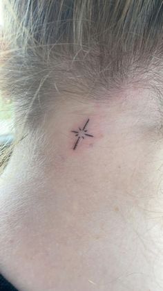 a small cross tattoo on the back of a woman's neck