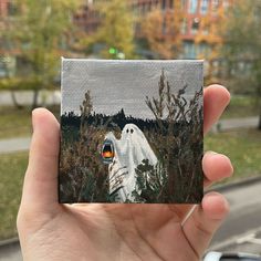 a hand holding up a piece of art that looks like a ghost in the woods