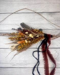 an arrangement of dried flowers and feathers on a white wooden background with red streamers