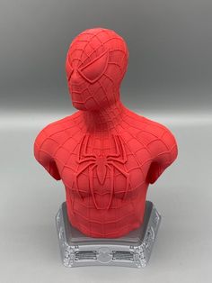 a red spider man busturine sitting on top of a plastic stand in front of a gray background