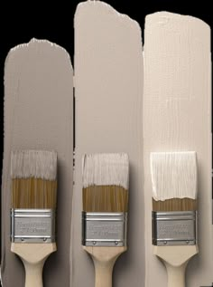 three paintbrushes are lined up against the wall, one is white and the other is beige