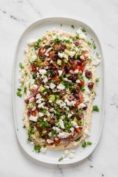 flatbread with black olives, feta cheese and herbs on a white plate