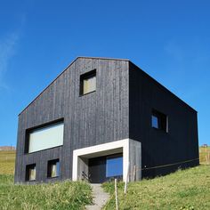 a black building with two windows on top of a grassy hill next to a fence