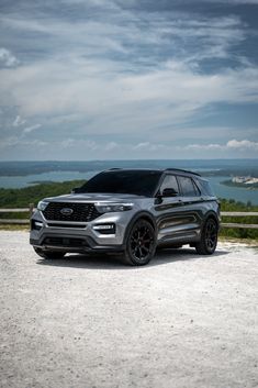 an suv parked on the side of a road next to a body of water with clouds in the background