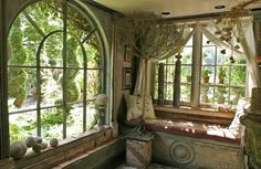 an old fashioned living room with large windows and lots of plants in the window sill