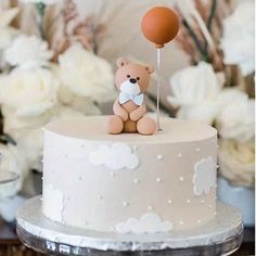 a small teddy bear sitting on top of a white cake with a balloon attached to it