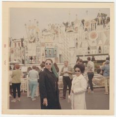 an old photo of two people standing in front of a roller coaster ride at the amusement park