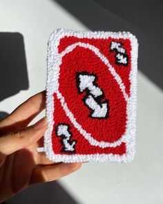 a hand holding up a crocheted patch with the letter s on it in red and white