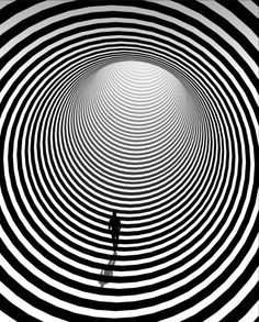 a man standing in the middle of a black and white tunnel with an optical pattern