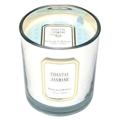 a white candle with a blue label on the lid that says coastal jasmine