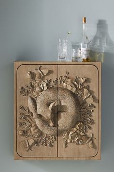 a wooden cabinet with an intricate carving on the front and sides, holding liquor bottles