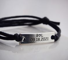 a close up of a bracelet with a metal tag attached to it on a white surface