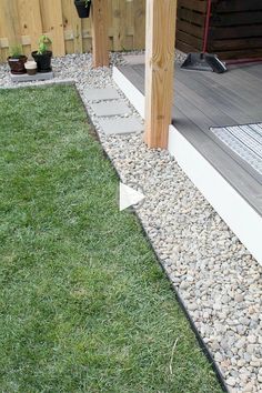 the side of a house with grass and rocks on it, next to a wooden deck