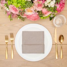 a place setting with flowers and silverware on a wooden table top, including a napkin