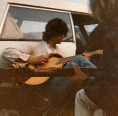 two men are playing guitars in front of a car