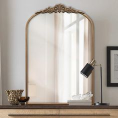 a mirror sitting on top of a wooden dresser next to a table with a lamp