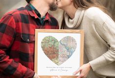 a man and woman kissing in front of a wooden frame with a map heart on it