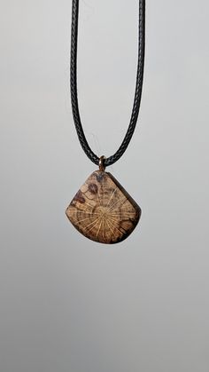 a wooden pendant hangs from a black cord on a gray background with a tree stump in the center