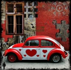 an old red and white car with hearts painted on it's side parked in front of a building