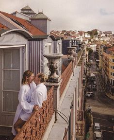 two women in bathrobes standing on a balcony next to buildings and looking at each other