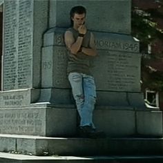 a man leaning against a monument talking on a cell phone while holding his hand up to his face