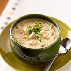 a green bowl filled with soup sitting on top of a yellow plate next to a spoon