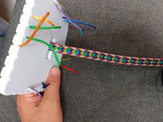 a person is holding a piece of paper with colorful cords attached to it and there are glasses on the table