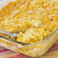 a casserole dish filled with corn and topped with a silver serving fork on a striped cloth