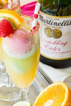 two glasses filled with colorful drinks next to oranges and raspberries