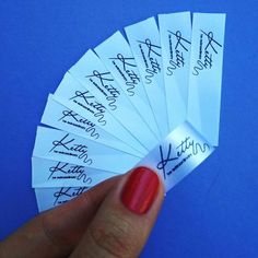 a person's hand holding six white paper tags with writing on them, in front of a blue background