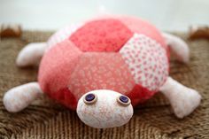 a red and white stuffed animal laying on top of a brown carpet next to a pink ball