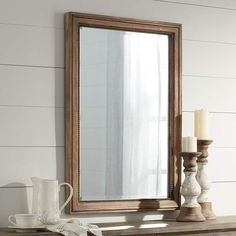 a mirror sitting on top of a wooden table next to a vase and candle holder