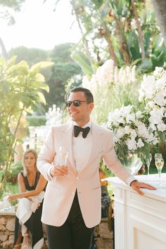 a man in a pink tuxedo standing next to a table with wine glasses