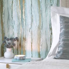 a bed with pillows and a vase on top of it next to a wall paper