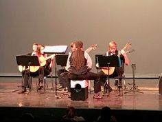 a group of people sitting on top of a stage next to each other playing musical instruments