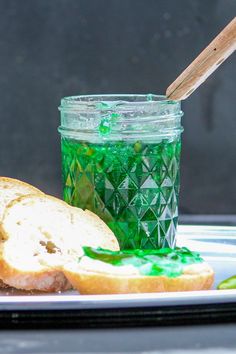 a sandwich on a plate next to a jar of green jelly and a wooden spoon