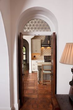 an archway leads into a kitchen with white cabinets and tile flooring, along with a lamp