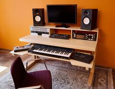 a computer desk with two monitors, keyboard and other musical equipment on it in front of an orange wall