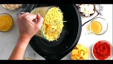 someone is making pasta in an electric skillet with ingredients around it and on the table